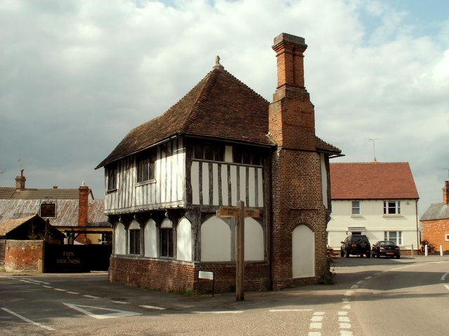 A historic half-timbered building with a large brick chimney at a road junction in a village.