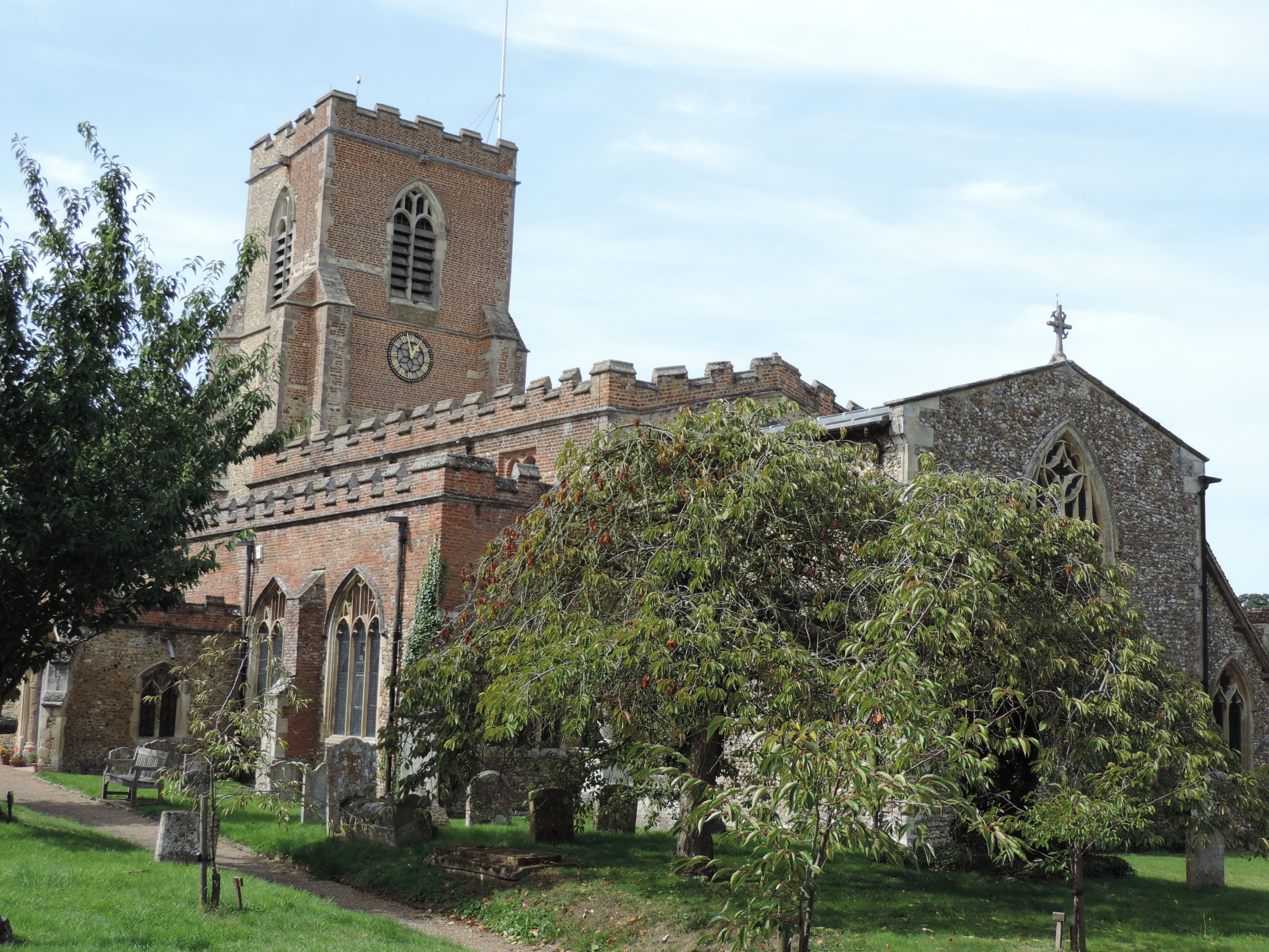 A historic stone church with a tall clock tower surrounded by trees and gravestones.