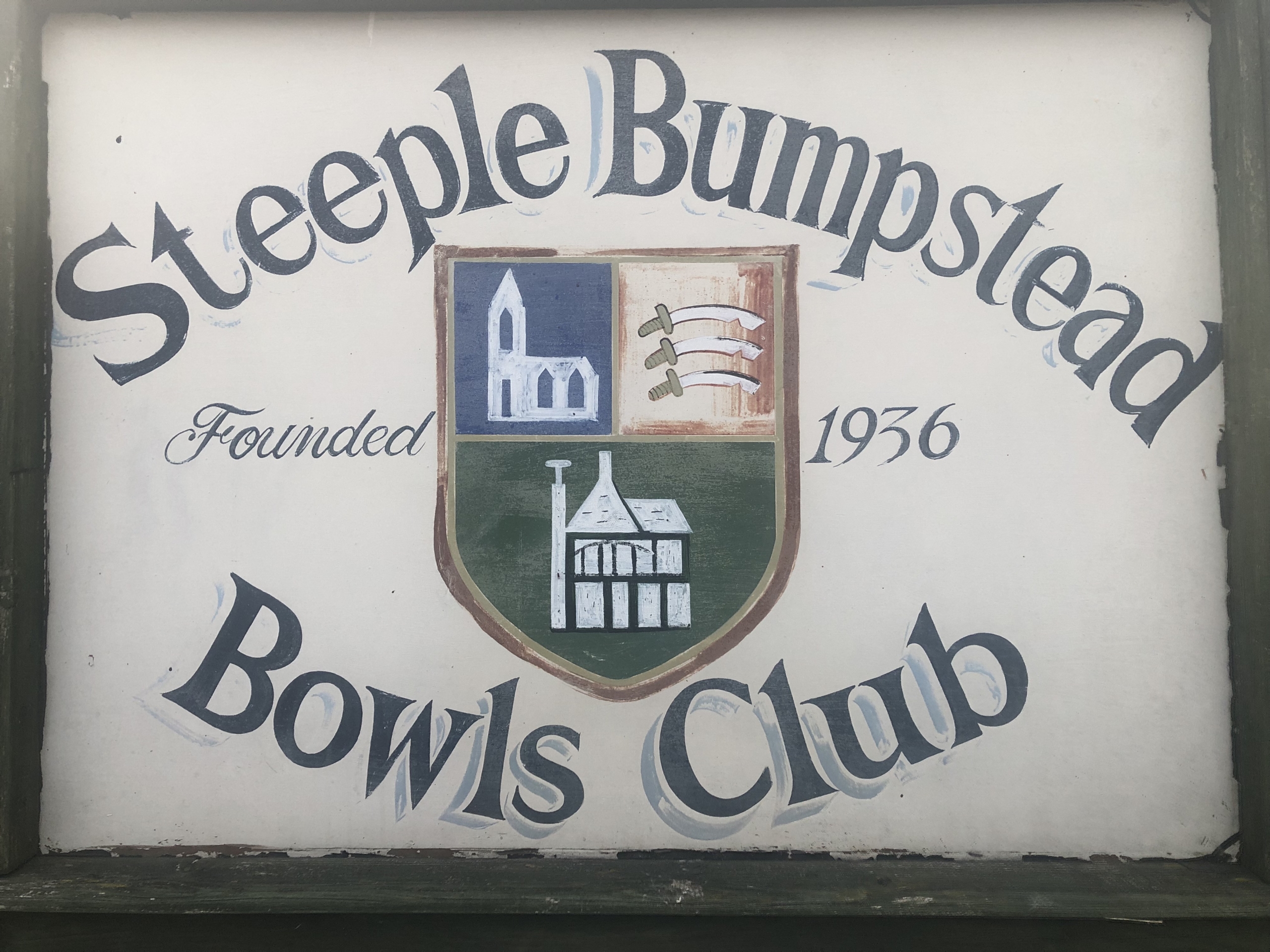 Sign for Steeple Bumpstead Bowls Club, founded 1936, with a shield showing buildings and three seaxes.