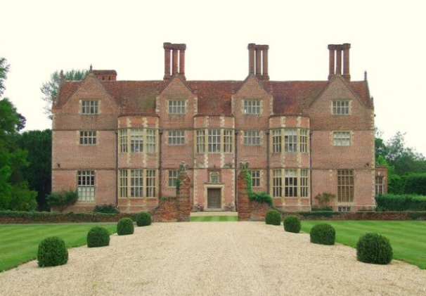 A large, historic brick mansion with tall chimneys and manicured gardens at the front.