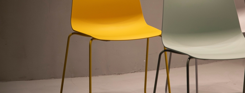 Three modern chairs, yellow, light green, and white, are arranged on a plain, light-coloured floor.