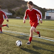 Three boys in red football kits running and playing football on an outdoor pitch.