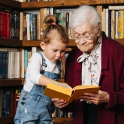 An elderly woman and a young girl read a book together in a library.