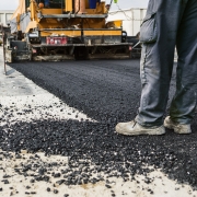 Close-up of workers surfacing a road with tarmac, machinery and fresh black tarmac visible.
