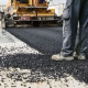 Close-up of workers surfacing a road with tarmac, machinery and fresh black tarmac visible.