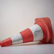 A worn orange and white traffic cone lying on its side against a plain white wall.