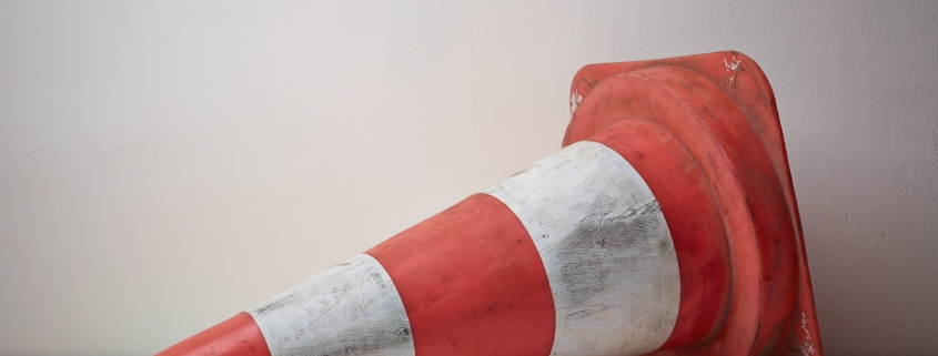 A worn orange and white traffic cone lying on its side against a plain white wall.