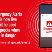 A smartphone displays an emergency alert; text warns the system will notify people of life-threatening dangers.