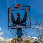 A village sign for Steeple Bumpstead featuring a black bird with outstretched wings against a blue sky.