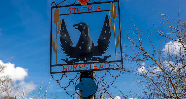 A village sign for Steeple Bumpstead featuring a black bird with outstretched wings against a blue sky.
