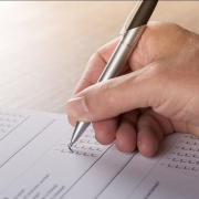 Hand holding a pen and filling out tickboxes on a paper form or survey on a wooden surface.