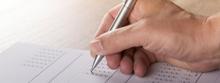 Hand holding a pen and filling out tickboxes on a paper form or survey on a wooden surface.