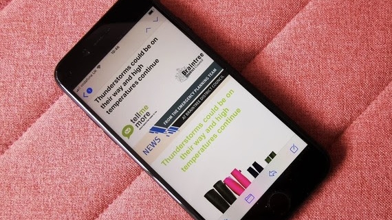 A smartphone on a pink fabric surface displays a news alert about potential thunderstorms and high temperatures.