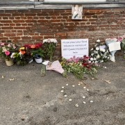 Flowers and a sign honouring Queen Elizabeth II are placed against a brick wall beneath her photo.