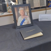 Framed portrait of Queen Elizabeth II and a book of condolence on a black tablecloth.