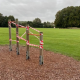 Outdoor exercise bars wrapped in red and white tape, with a grassy field and trees in the background.