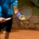 A tennis player prepares to serve on a clay court, holding a racquet and tennis ball.