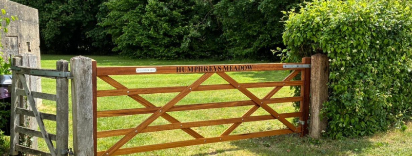A wooden gate labelled "HUMPHREYS MEADOW" opens to a grassy field with trees and greenery behind it.